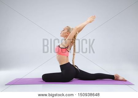 Young blonde slim girl is stretching in the studio on the white background