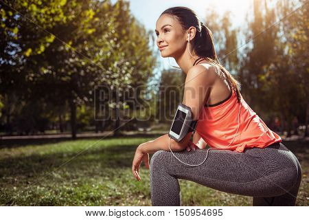 Listen and prepare. Beautiful young girl doing her morning exercises preparing for running while listening to music using her smartphone.