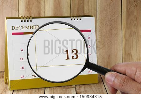 Magnifying glass in hand on calendar you can look Thirteenth date of monthFocus number Thirteen in DecemberConcept in business and meetings.