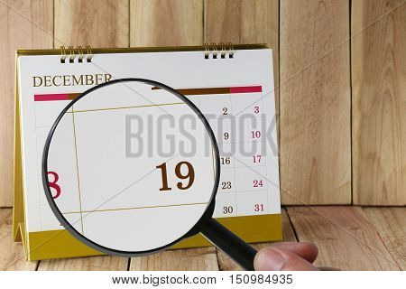 Magnifying glass in hand on calendar you can look Nineteenth date of monthFocus number nineteen in DecemberConcept in business and meetings.