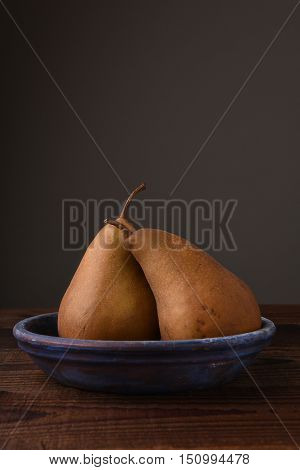 Two Bosc pears on a blue plate on wood table. Vertical format on gray background with copy space,