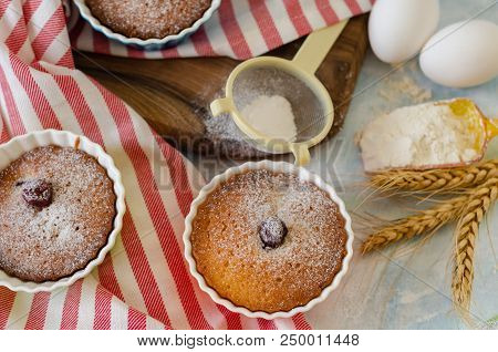 Cakes With Cerries On A Table In Small Porcelain Cups .there Are  Eggs, Flour, Wheat, Powdered Sugar