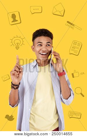 Great Idea. Cheerful Young Blogger Pointing His Finger Up And Smiling While Talking On The Phone