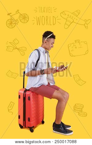 Web Money. Positive Modern Teenager Sitting Comfortably On His Big Suitcase And Looking At The Scree