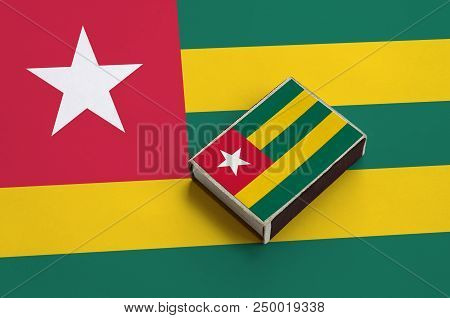 Togo Flag  Is Pictured On A Matchbox That Lies On A Large Flag.