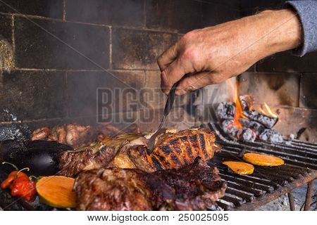 Man Making Barbecue For The Lunch. Meat Cuts And Vegetables Warming On The Embers On An Iron Grill. 