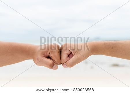 Men Hands Fist Bumping Together On Blurred Sea And Sky Background. Friendship Day Concept.