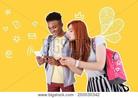 Looking Curious. Two Friends Standing And Holding Modern Smartphones While Sending Party Invitations