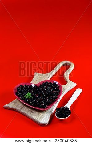 Organic Black Raspberry On A Decorative Red Plate In The Form Of A Heart. Blue Background. Top View.