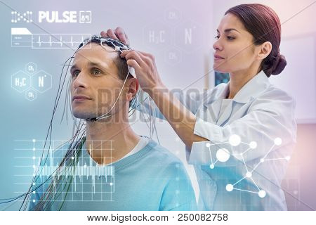 Checking Wires For Eeg. Young Man Looking Calm While A Careful Nurse Doing Necessary Preparations Fo
