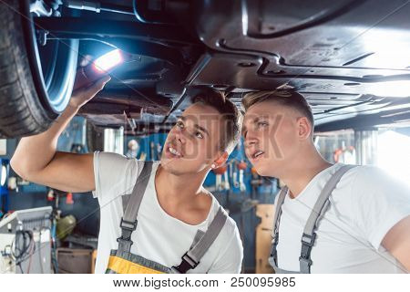 Two skilled auto mechanics analyzing together the rims of a lifted car while working in a modern automobile repair shop