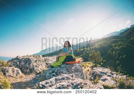 A Woman Is Sitting In A Sleeping Bag On Top Of A Mountain. A Smiling Girl Rests After A Climb. The B