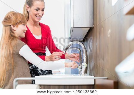 Happy mother and her cute daughter comparing together two different bathroom sinks in a modern sanitary ware shop with various products for sale