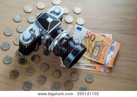 Euro Banknotes, Coins And A Camera On A Light Wooden Background.