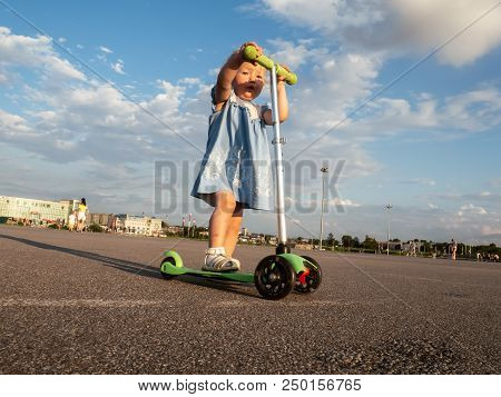 Street Sport: Happy Girl In Riding A Kick Scooter On The Pavement And Puddles. Portrait.