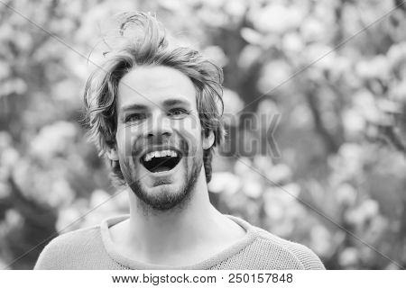 Man Smile In Park With Blossoming Trees. Guy With Beard Smiling In Yellow Sweater On Floral Backgrou
