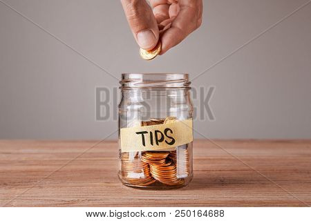 Tips. Glass Jar With Coins And An Inscription Tips. Man Holds  Coin In His Hand.