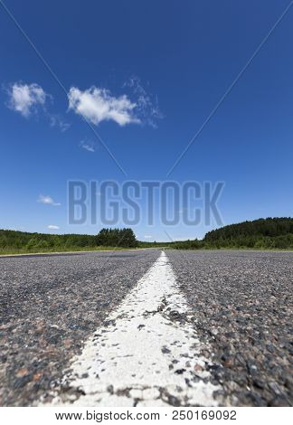 Empty Asphalt Road With A White Strip Of Road Markings, A Photo In The Summer With A Blue Sky And Cl