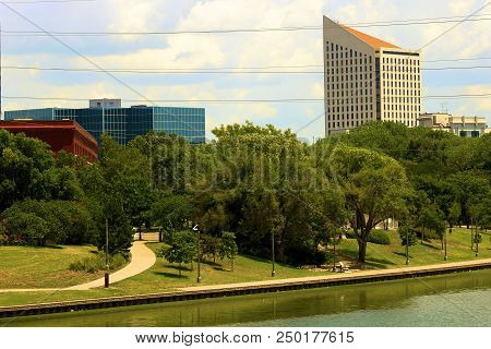 July 15, 2018 In Wichita, Ks:  Riverwalk Pathway Besides A Park With Manicured Gardens And The Arkan