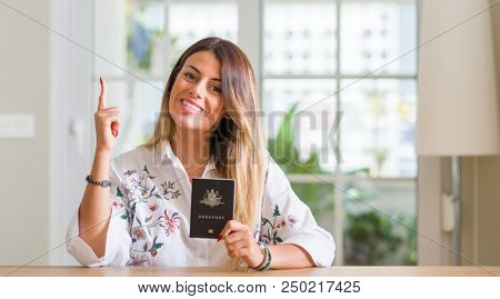 Young woman at home holding a passport of Australia surprised with an idea or question pointing finger with happy face, number one