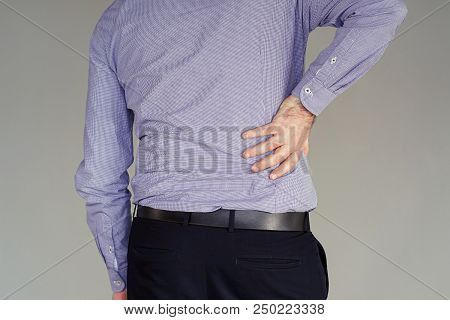 Close-up View Of A Young Man With Pain In Kidneys On Gray Background. Businessman With Back Ache Cla