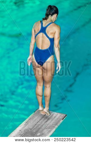 Female Diver Standing On The Jumping Board. Preparing To Jump Into The Pool