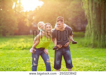 Family Piggyback -parents Playing With Their Children In The Park