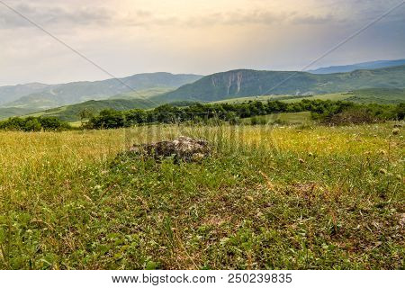 Green Meadow On The Background With Distant Mountains. Open Field With Green Grass. Landscape Photog