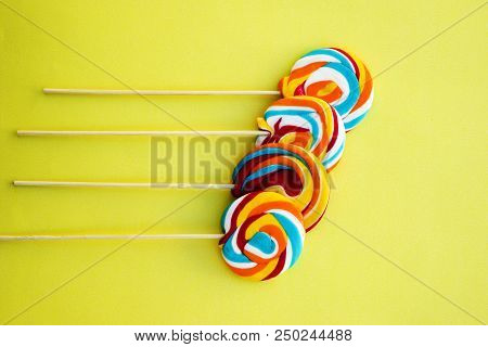 Colorful Hard Candy Lollipop On Yellow Pastel Background. Rainbow Sweet Pattern On Stick Flying Arou