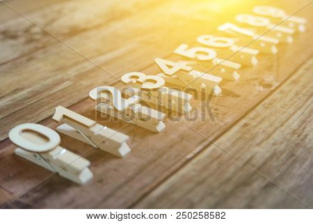 Clothpin With Number Of 0,1,2,3,4,5,6,7,8, And 9 In A Row With Sun Flare And Wooden Background.