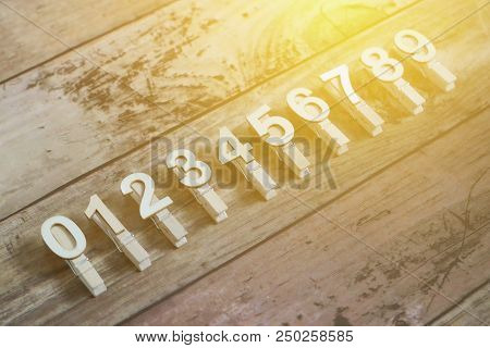 Clothpin With Number Of 0,1,2,3,4,5,6,7,8, And 9 In A Row With Sun Flare And Wooden Background.