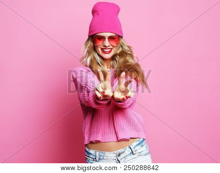 Stylish fashion portrait of trendy casual young woman in pink pulover and hat, posing over pink background. Hipster style.