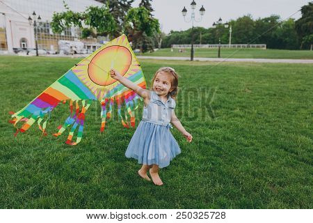 Joyful Little Cute Child Baby Girl In Denim Dress Running, Play With Colorful Kite And Have Fun In G