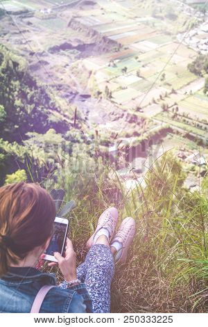 Successful Woman Hiker Using Smartphone At Cliff Edge On Mountain Top. Bali Island. Indonesia.