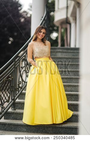 Lady In Yellow Erening Dress Stand On Stairs.