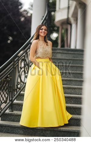 Lady In Yellow Erening Dress Stand On Stairs.