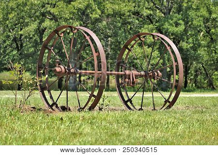Two Old Rusty Planter Wheels And Axle Sitting In A Green Country Field.