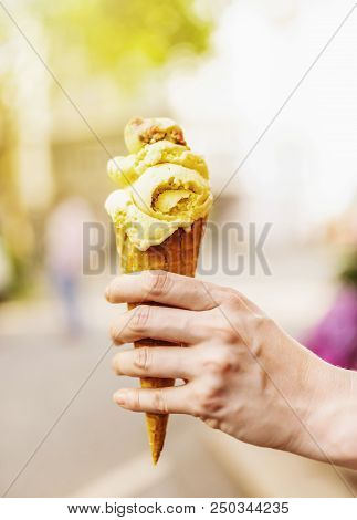Female Hand Holding Ice Cream Cone Against Blurred Background