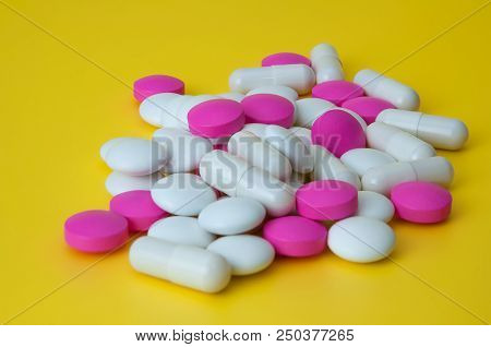 A Pile Of Pills Of Different Colors On A Yellow Background.