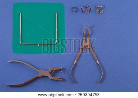 Tools For Installing The Cofferdam. Rubberdam And Clamp Lying On The Table A Blue Background.