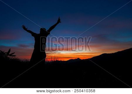 Silhouette Of Traveler With Hands Up In The Sunset On The Mountain