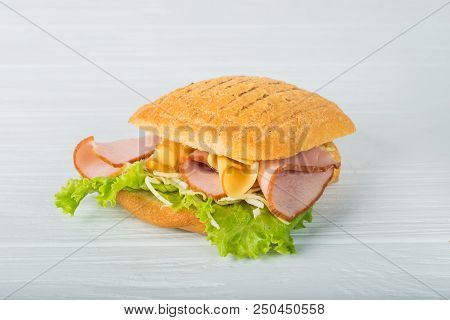 Pressed And Toasted Double Panini With Ham And Cheese Served On Sandwich Paper On A Wooden Table