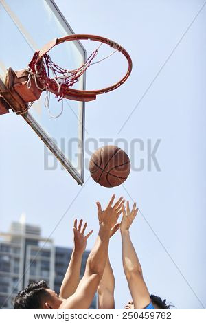 Young Asian Adults Going Up For Rebounds On Outdoor Basketball Court.