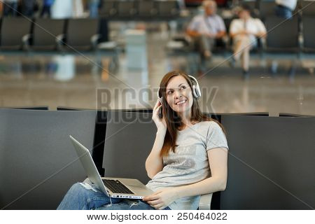 Young Pensive Traveler Tourist Woman With Headphones Listening Music Working On Laptop, Wait In Lobb