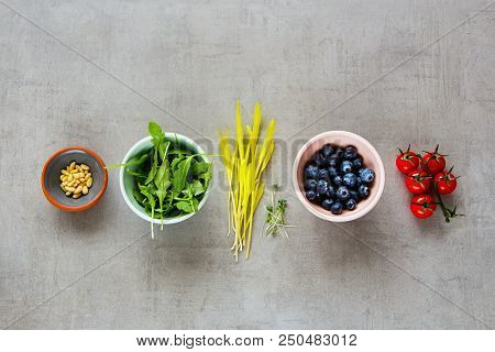 Various Raw Organic Food: Arugula, Cress Salad, Blueberries, Cherry Tomatoes, Pine Nuts Over Light B