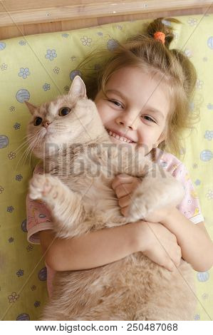 Little Girl Hugging A Cat Lying On A Mattress On The Floor