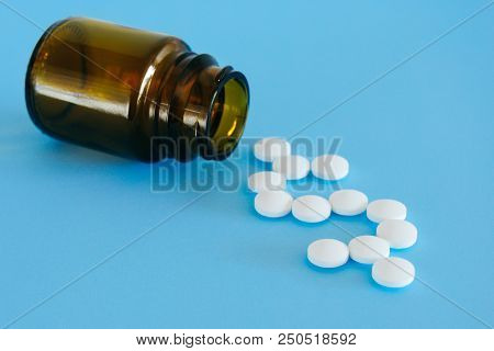 White Pills Spilling From A Medicine Bottle Forming A Dollar Sign On A Blue Background.