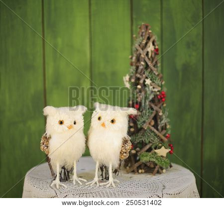 Two Christmas Owls On A Table Near A Decorative Christmas Tree On A Green Background. New Year Greet