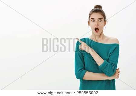 Studio Shot Of Impressed Happy Joyful Girl With Bun Hairstyle In Stylish Loose Sweater, Dropping Jaw