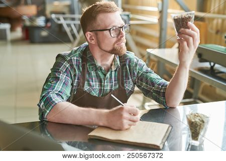 Portrait Of Modern Bearded  Barista Holding Glass Of Coffee Beans While Checking Quality Of Roast In
